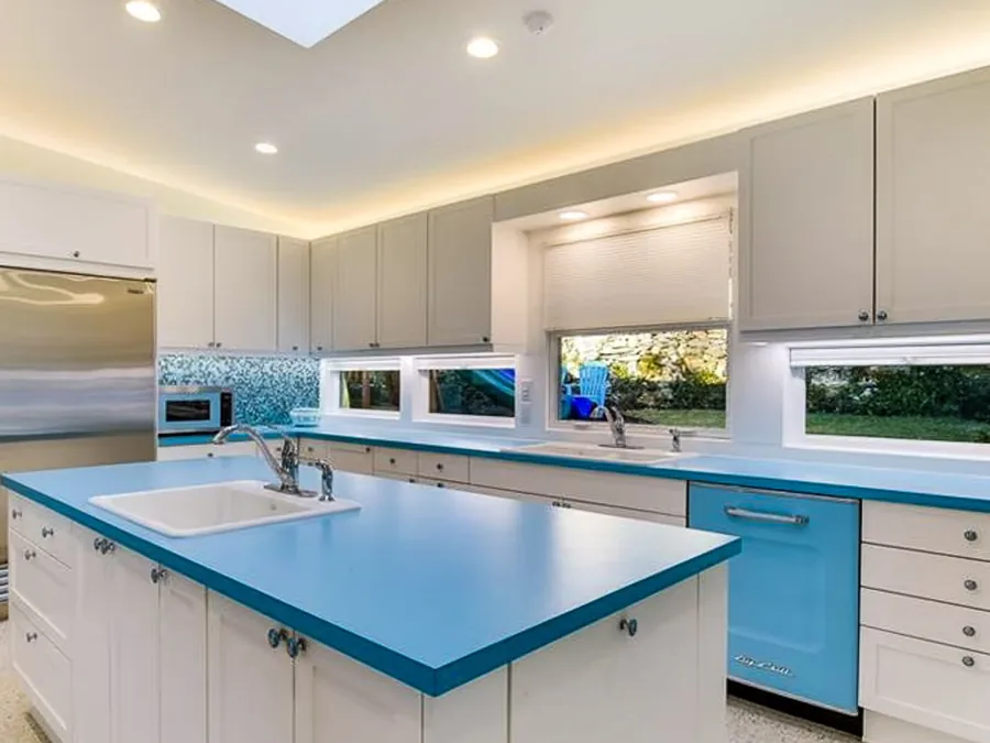The Balcones kitchen before work, with white cabinets, blue worktops, a strip of small windows and a skylight in the sloped ceiling.