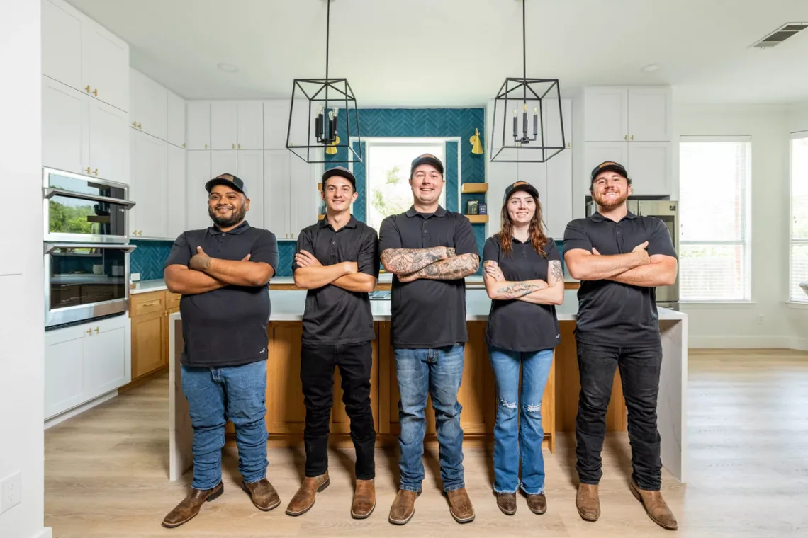 The five-person Fit Build Construction crew standing together in a finished kitchen with a teal tile backsplash.