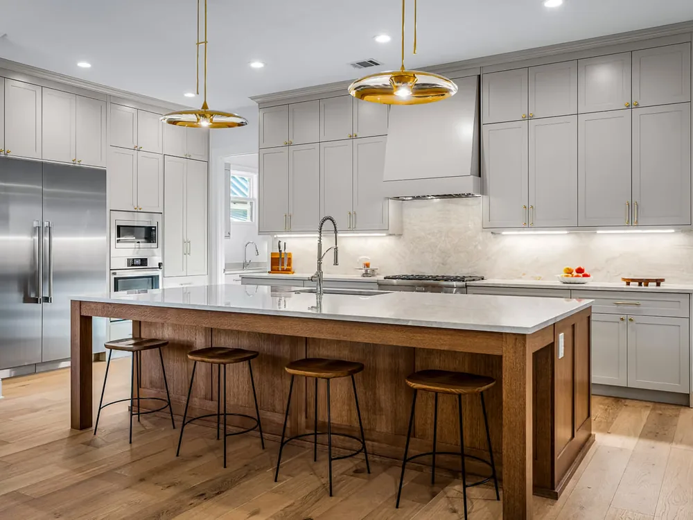 Remodeled Townes kitchen with pale grey cabinetry, brass pendant lights and a wood island with stools.